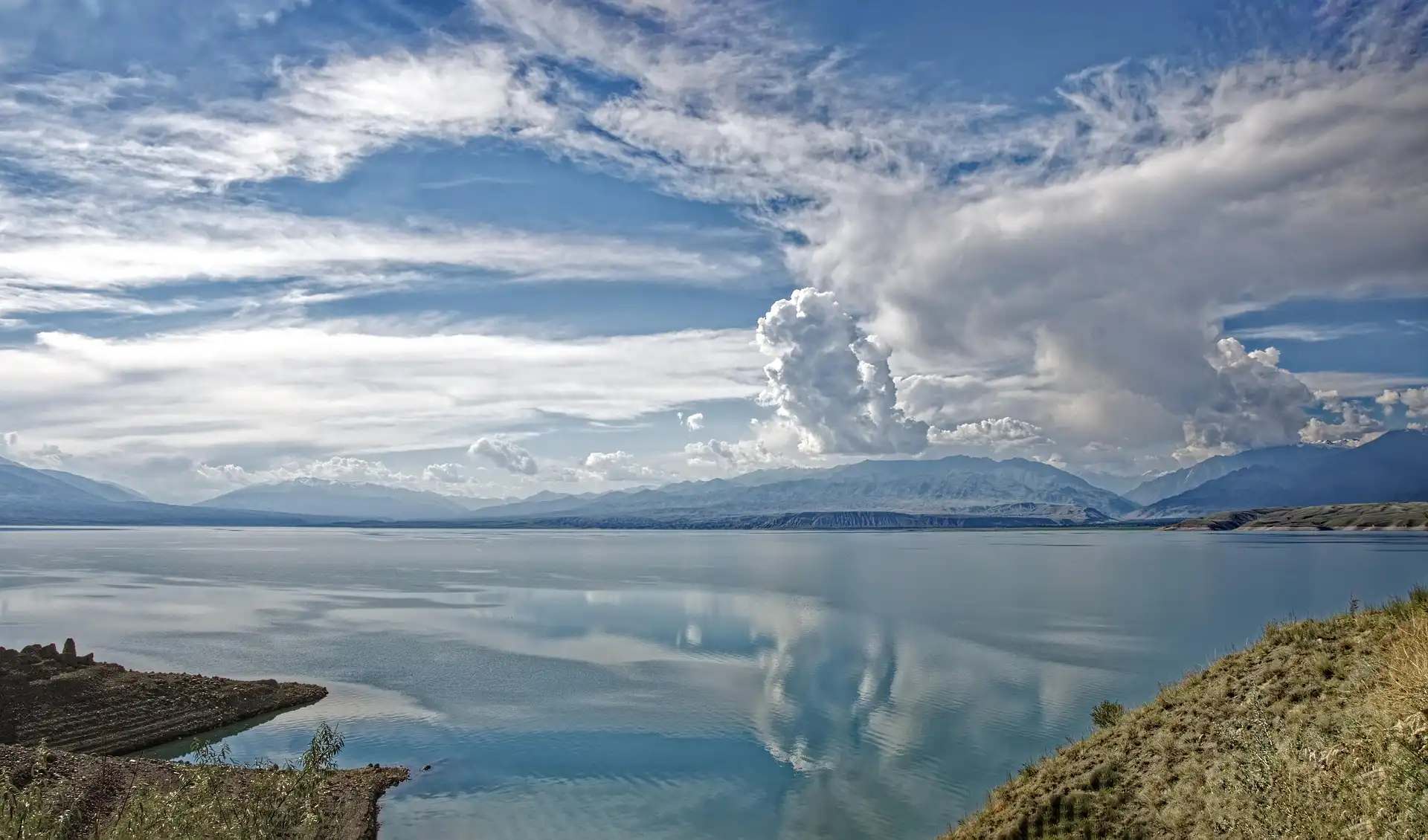 A mountain lake in Kyrgyzstan beneath a wide clouded sky.